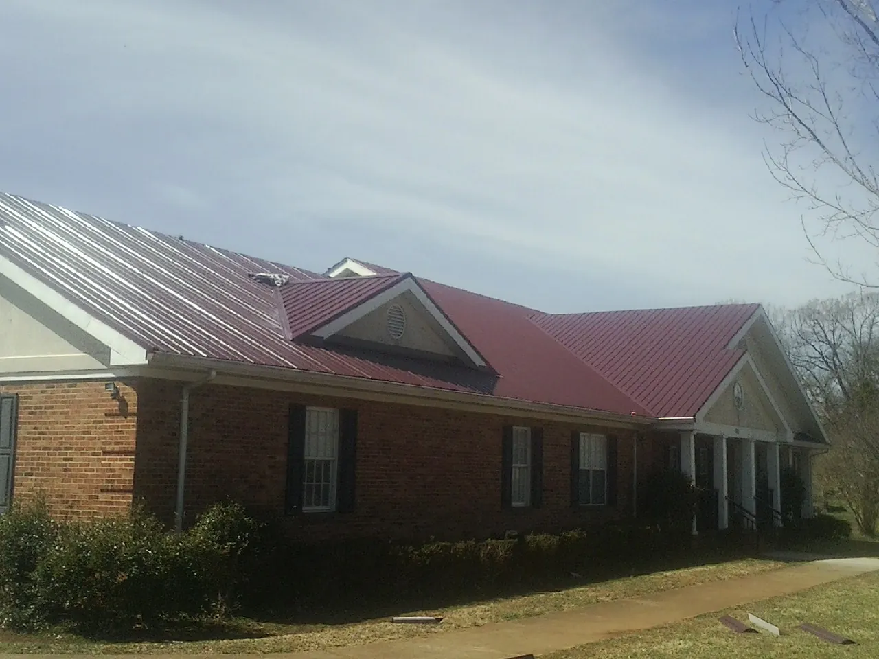 Red metal roof with gabled entries on a long brick building, from a Hail Damage Roof Repair job in Hingham