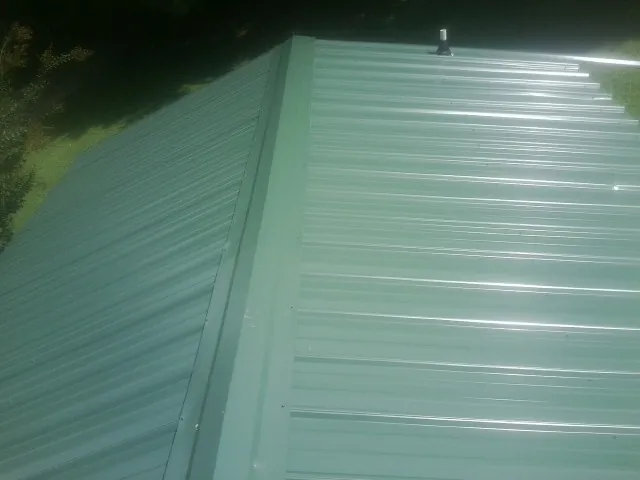 New green metal panels meeting at the ridge of a roof — Flat Roof Repair work by our crew in Hingham