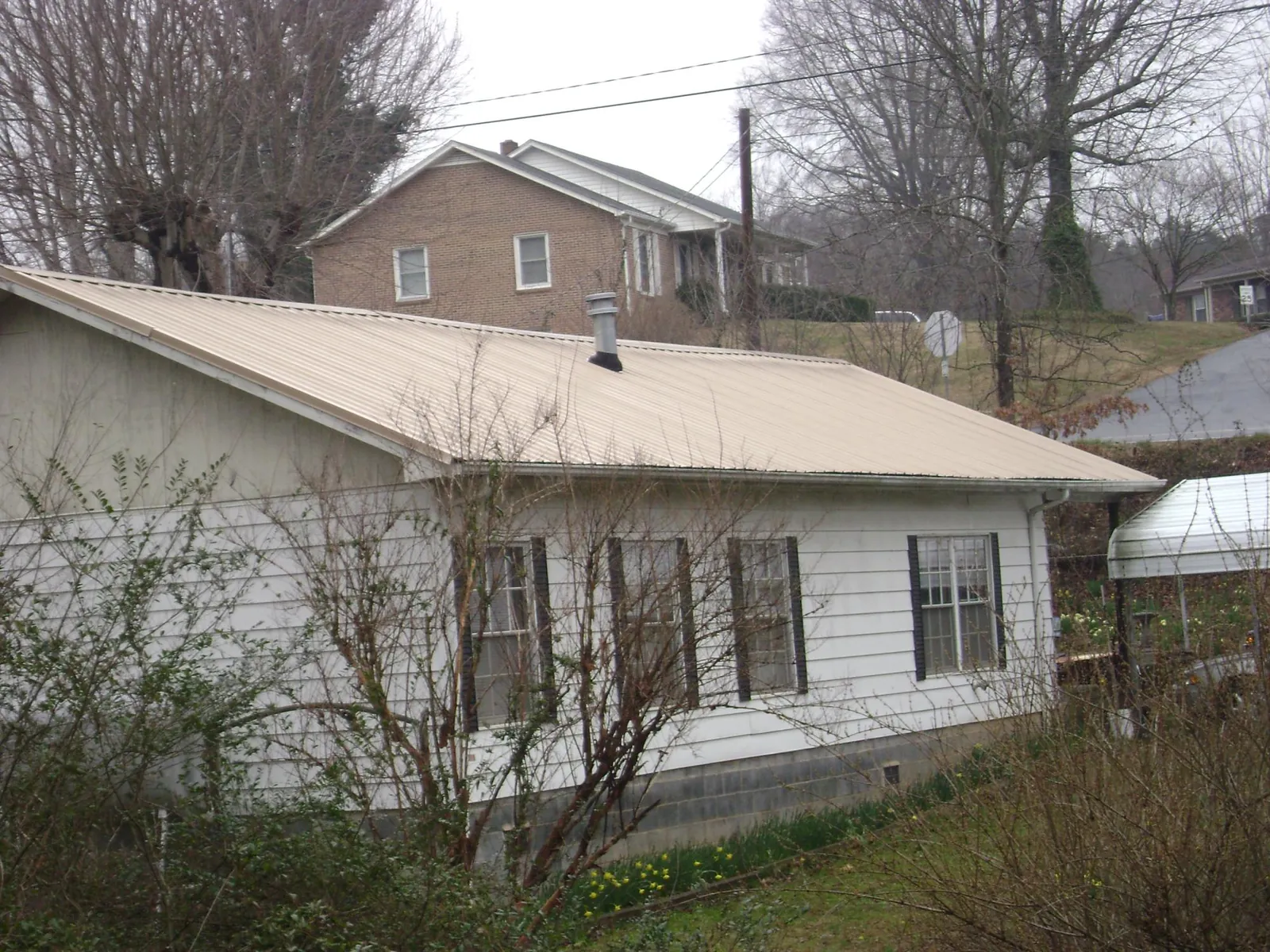 Tan metal roof on a white sided house set into a hillside — Commercial Roofing by Roofing Brothers in Hingham