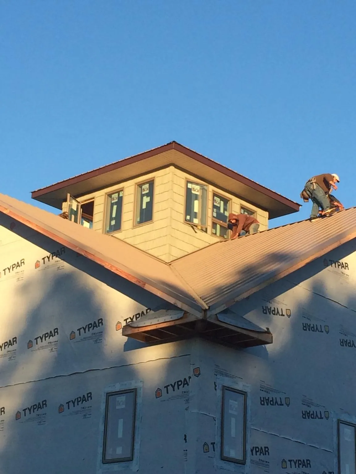 Roofers working around a rooftop cupola on a new metal roof at sunset — Roof Waterproofing in Hingham by Roofing Brothers